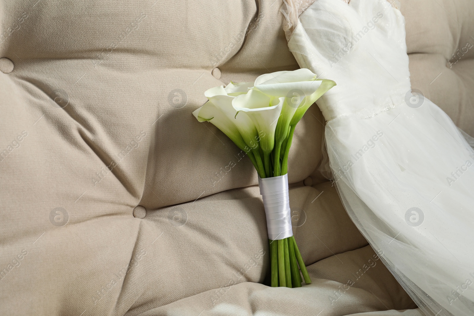 Photo of Beautiful calla lily flowers tied with ribbon and wedding dress on sofa