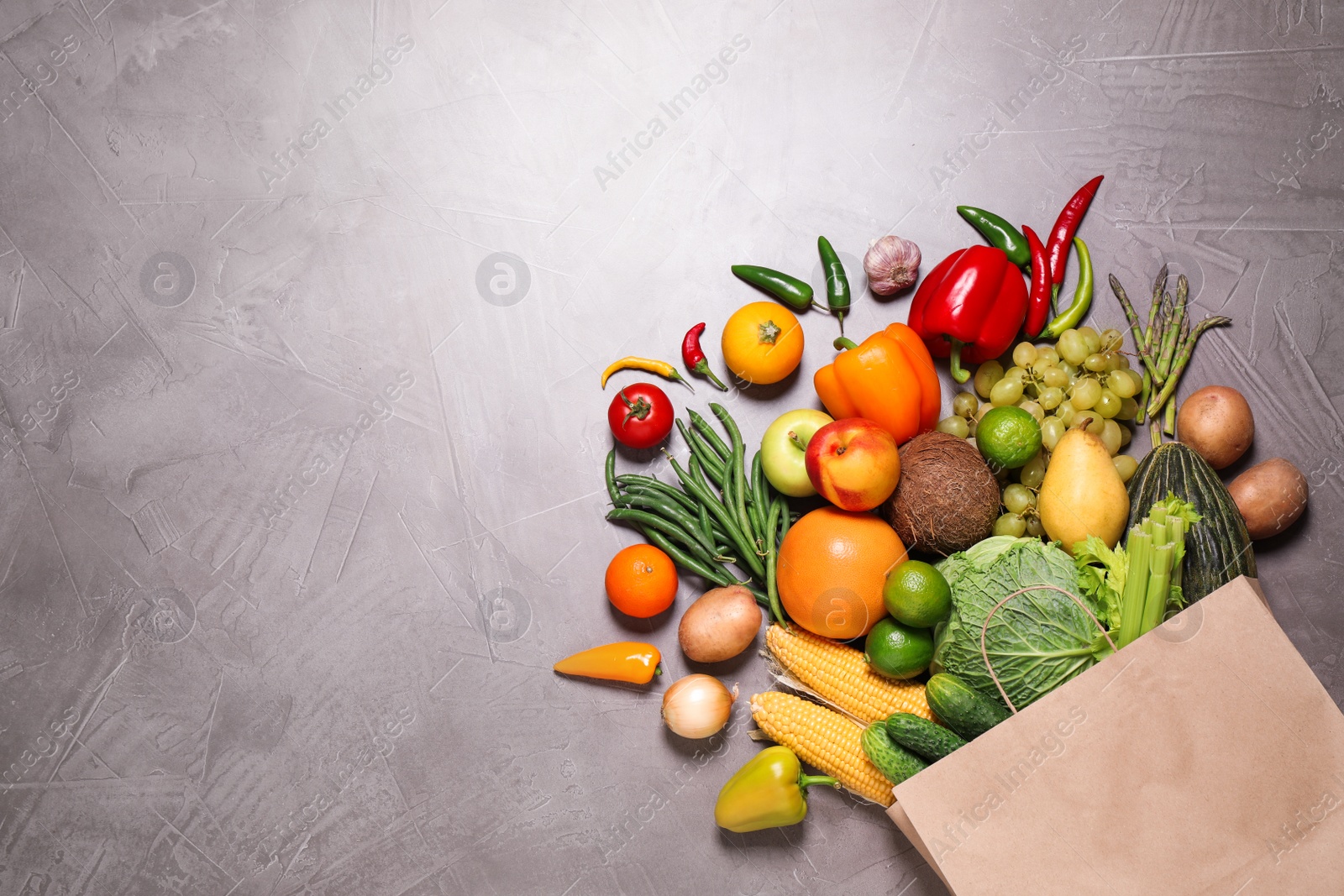 Photo of Paper bag with assortment of fresh organic fruits and vegetables on grey table, flat lay. Space for text