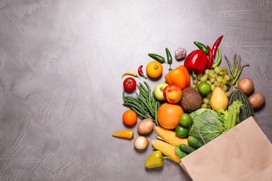 Photo of Paper bag with assortment of fresh organic fruits and vegetables on grey table, flat lay. Space for text