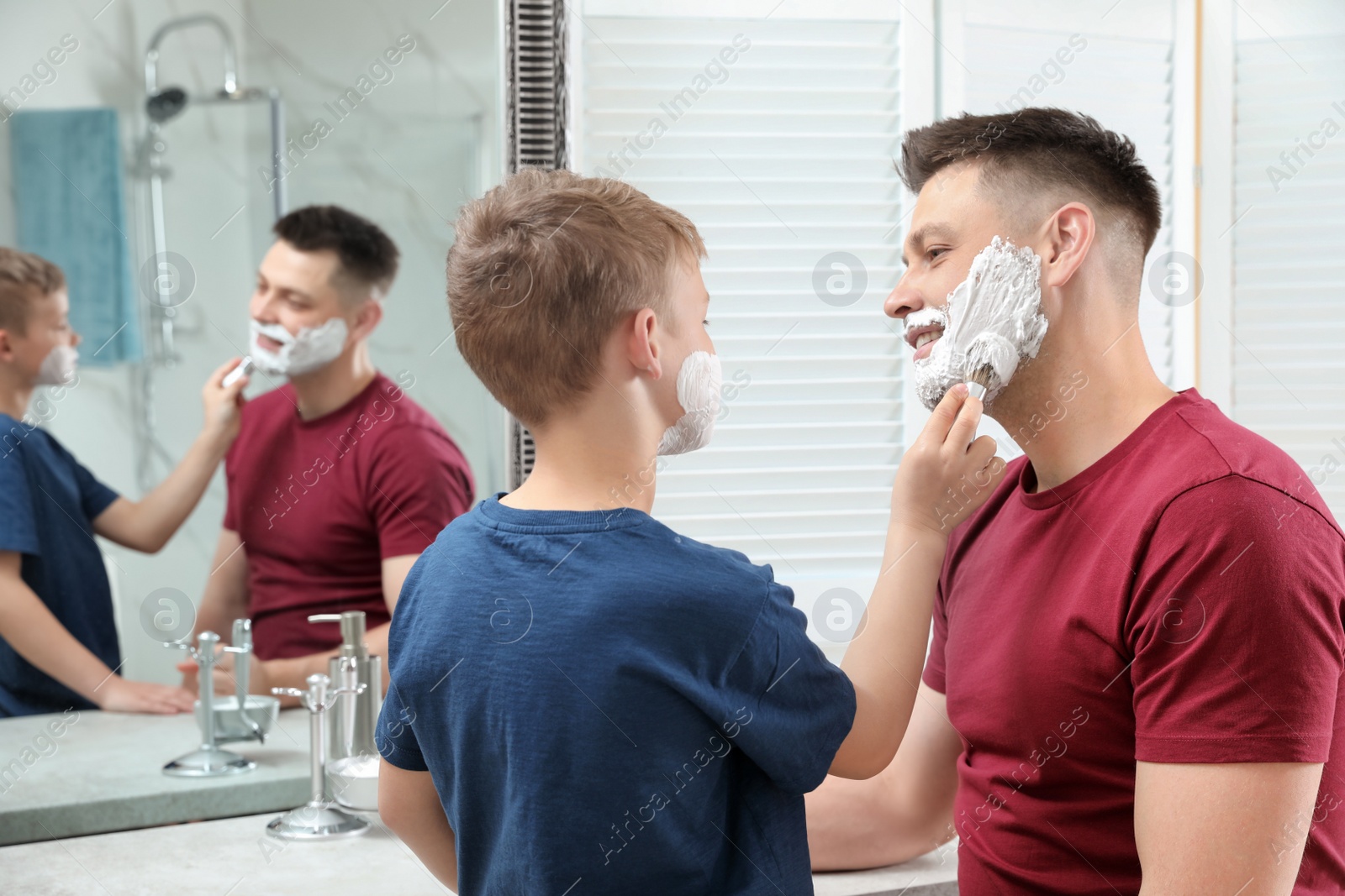 Photo of Son applying shaving foam on dad's face at mirror in bathroom