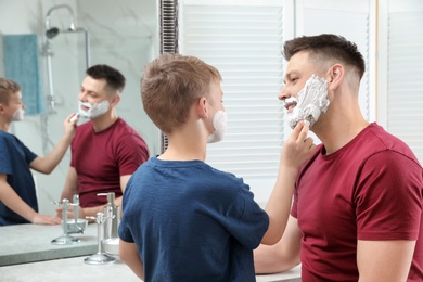 Son applying shaving foam on dad's face at mirror in bathroom