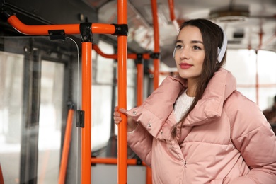 Photo of Beautiful young woman listening to music with headphones in public transport. Space for text