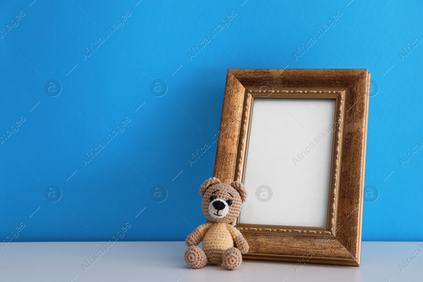 Photo of Empty photo frame and toy bear on white table near light blue wall. Space for design