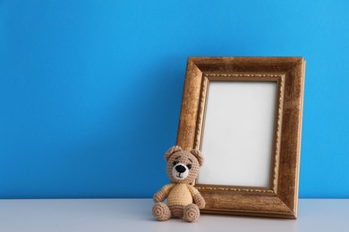 Empty photo frame and toy bear on white table near light blue wall. Space for design