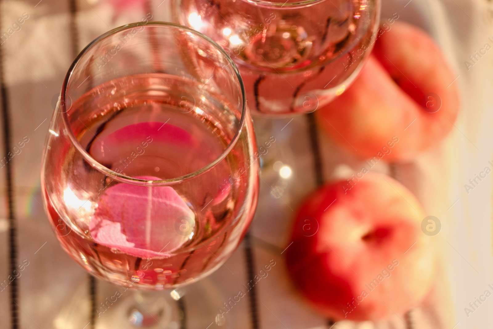 Photo of Glass of delicious rose wine with petals and peaches on white picnic blanket, closeup. Space for text