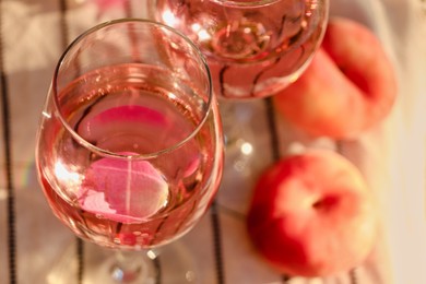 Photo of Glass of delicious rose wine with petals and peaches on white picnic blanket, closeup. Space for text