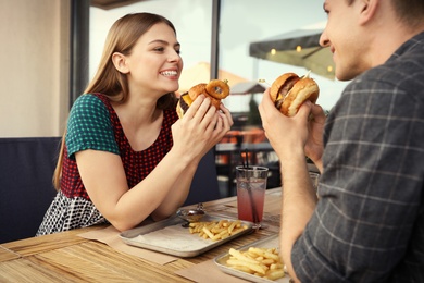 Photo of Young couple eating burgers in street cafe