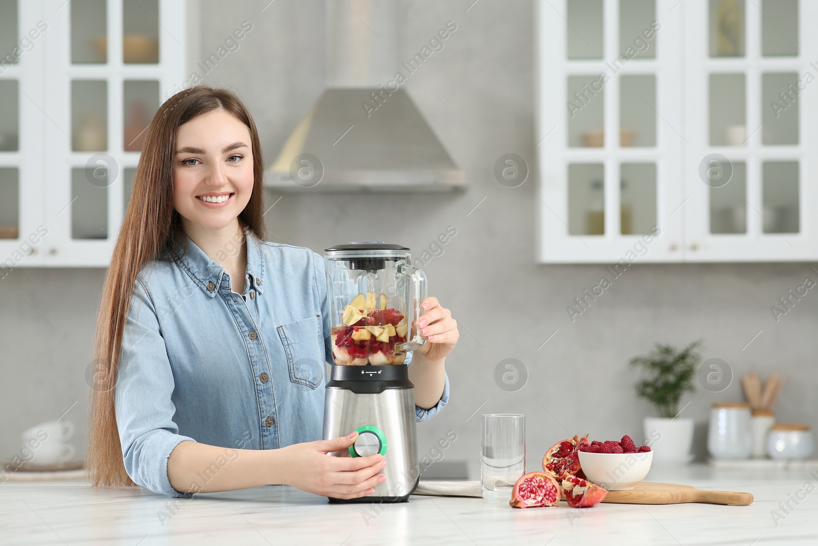 Photo of Beautiful young woman preparing tasty smoothie at white table in kitchen. Space for text