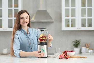 Photo of Beautiful young woman preparing tasty smoothie at white table in kitchen. Space for text
