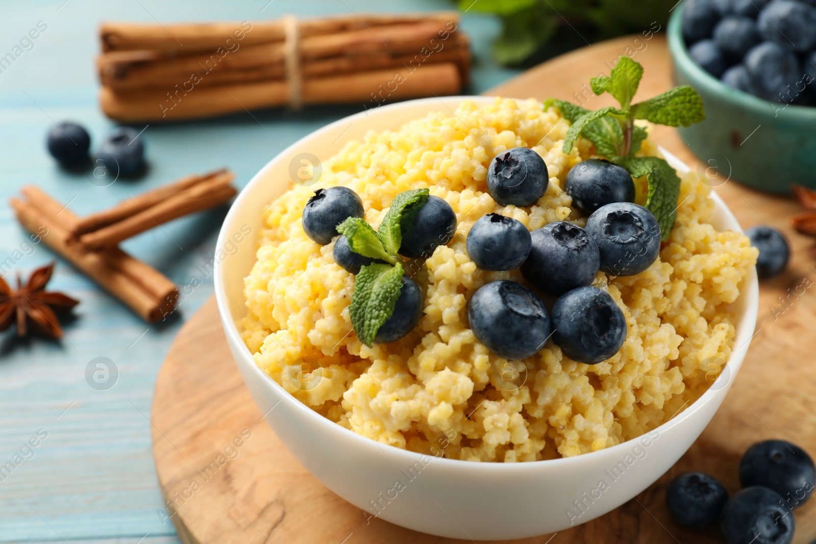 Photo of Tasty millet porridge with blueberries and mint in bowl on light blue wooden table, closeup