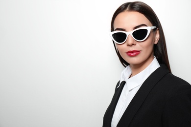 Photo of Young businesswoman in stylish sunglasses on light background, space for text