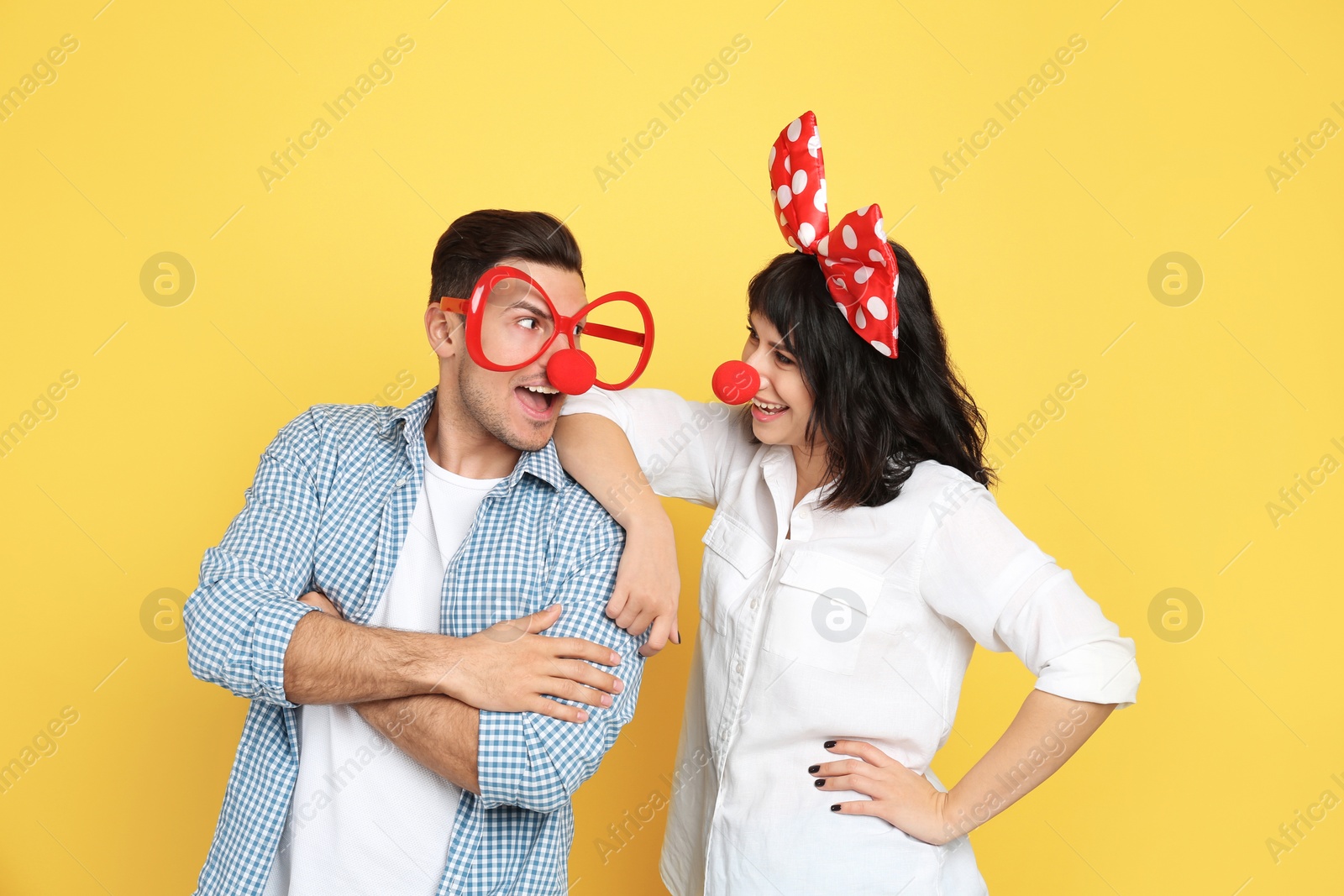 Photo of Couple with funny accessories on yellow background. April fool's day