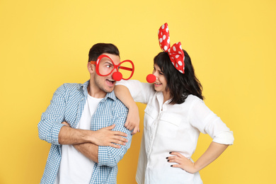 Photo of Couple with funny accessories on yellow background. April fool's day