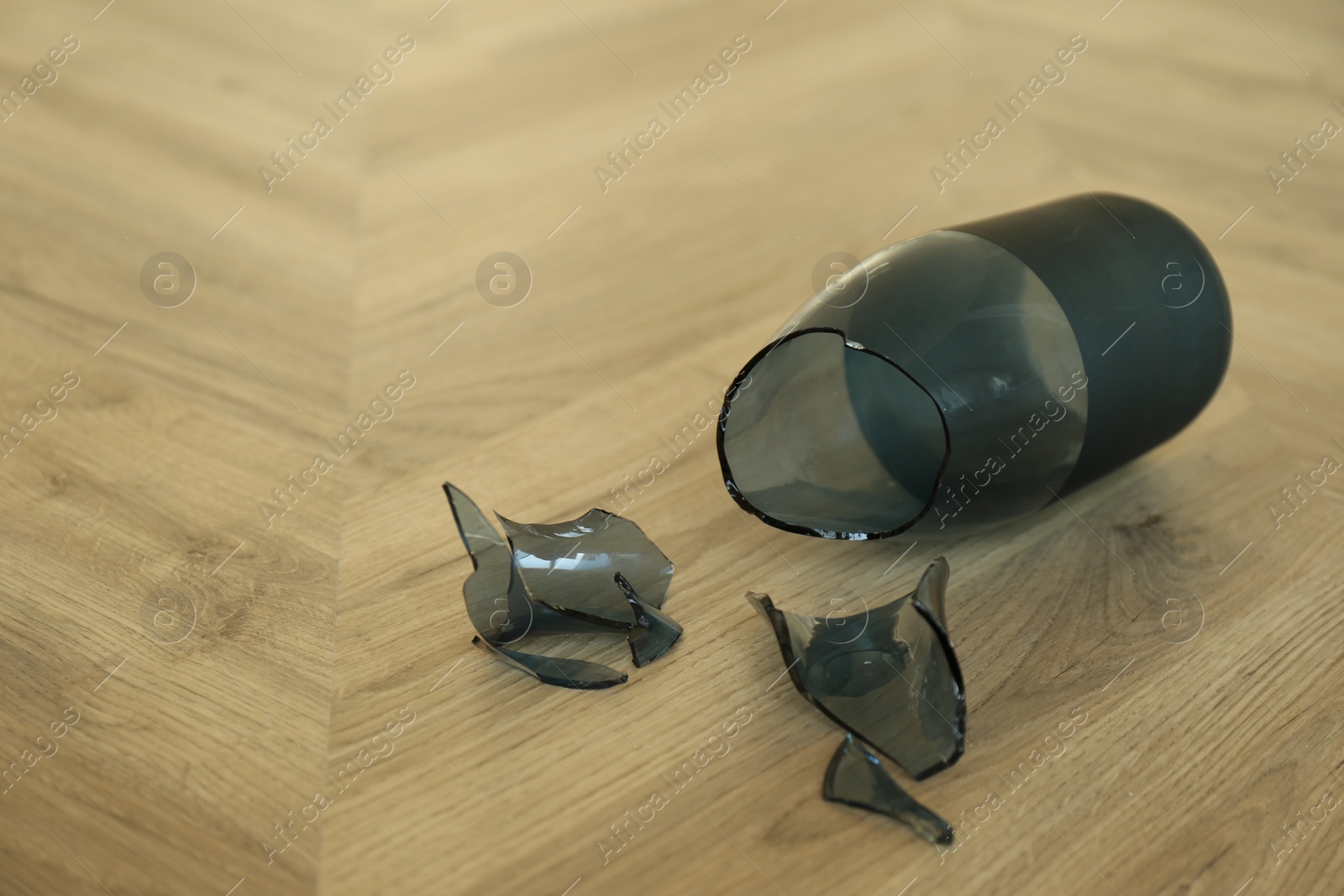 Photo of Broken blue glass vase on wooden floor. Space for text