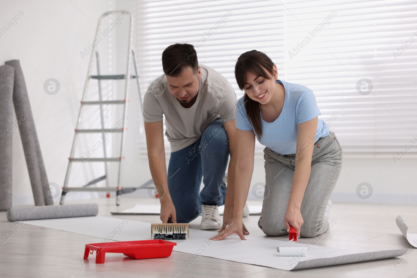 Photo of Couple applying glue onto wallpaper sheet in room