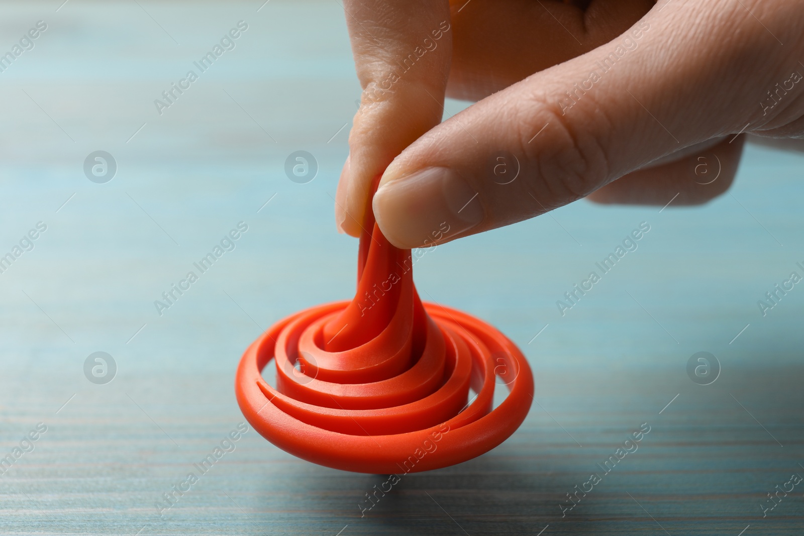 Photo of Woman playing with red spinning top at light blue wooden table, closeup