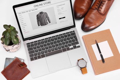 Photo of Online store website on laptop screen. Computer, stationery, credit cards, men's shoes and accessories on white background, above view