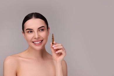 Photo of Beautiful young woman holding skincare ampoule on grey background. Space for text