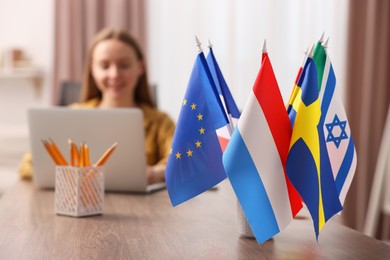 Photo of Woman working with laptop at table indoors, focus on different flags