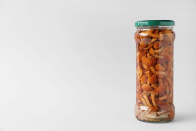 Jar of pickled mushrooms on light grey background. Space for text