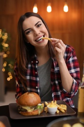 Young woman eating french fries and tasty burger in cafe