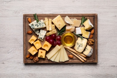 Photo of Cheese plate with honey, grapes and nuts on white table, flat lay