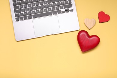 Photo of Long-distance relationship concept. Laptop and decorative hearts on pale yellow background, flat lay with space for text
