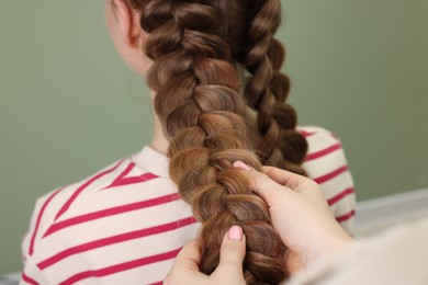 Photo of Professional stylist braiding woman's hair on olive background, closeup