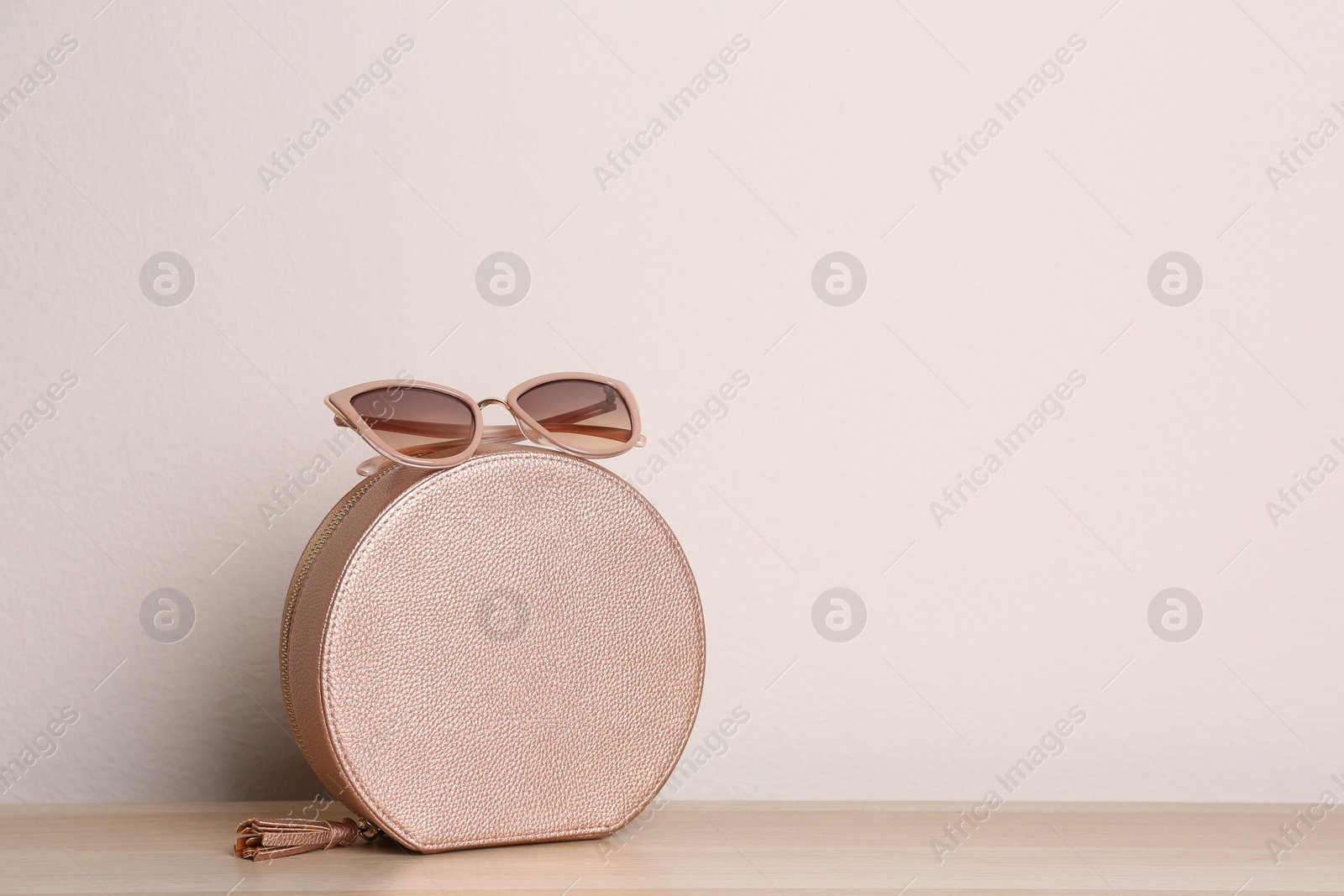 Photo of Stylish woman's bag and sunglasses on wooden table. Space for text