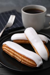 Photo of Delicious eclairs covered with glaze and coffee on grey wooden table