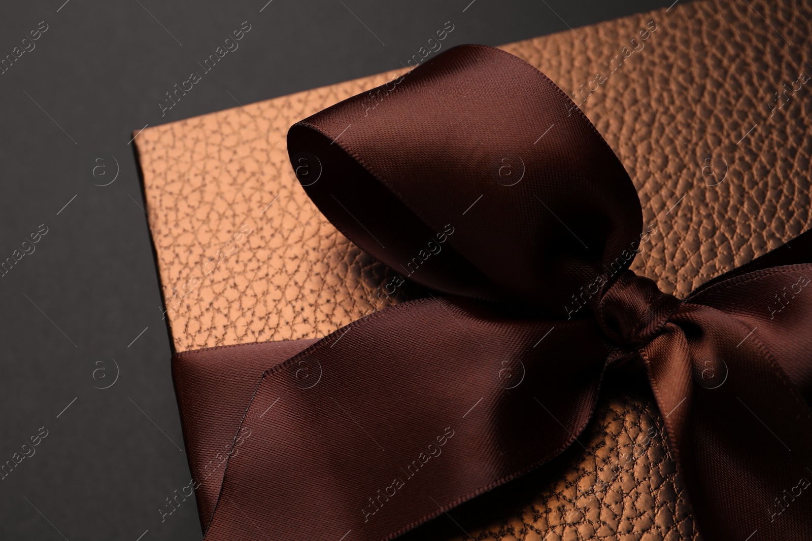 Photo of Brown gift box decorated with satin bow on black background, closeup