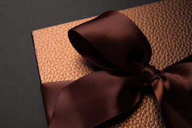 Photo of Brown gift box decorated with satin bow on black background, closeup