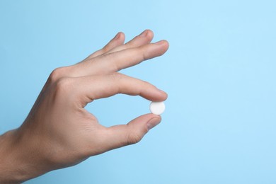 Man holding pill on light blue background, closeup