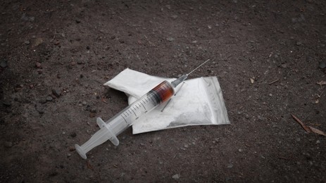 Photo of Plastic bags with powder and syringe on asphalt. Hard drugs