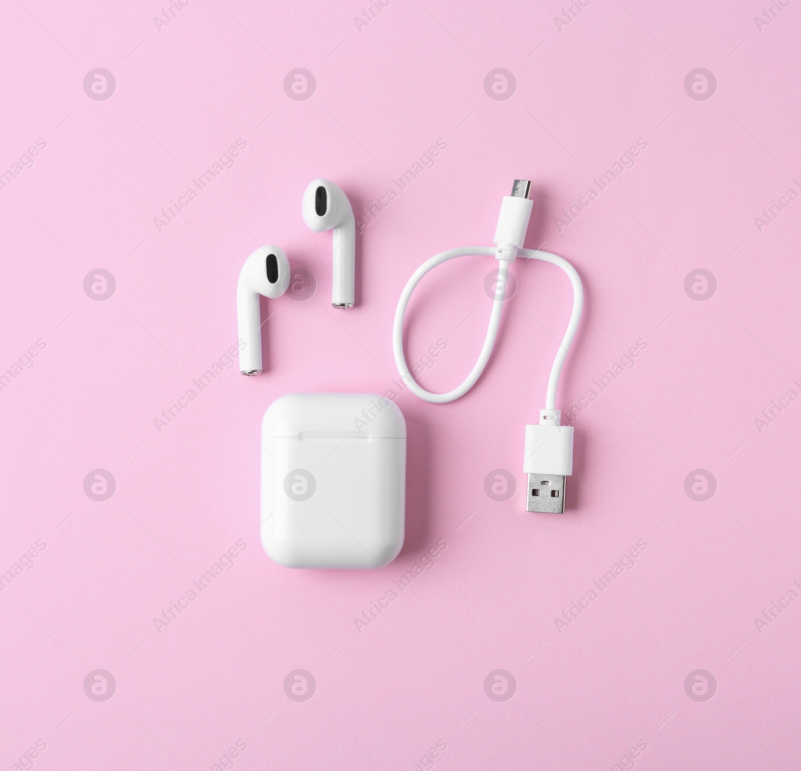 Photo of Modern wireless earphones and charging case with cable on pink background, flat lay