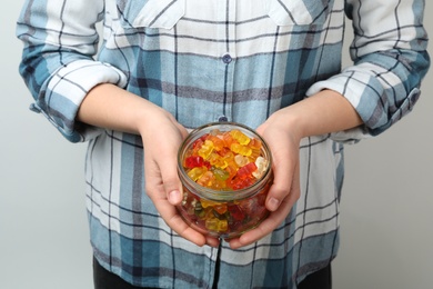 Photo of Woman holding jar of colorful jelly bears on light background, closeup