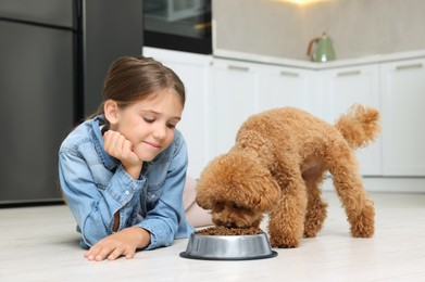 Photo of Little child feeding cute puppy in kitchen. Lovely pet
