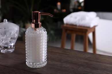 Photo of Dispenser with liquid soap on wooden table in bathroom, space for text