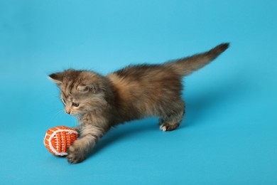 Photo of Cute kitten playing with ball on light blue background