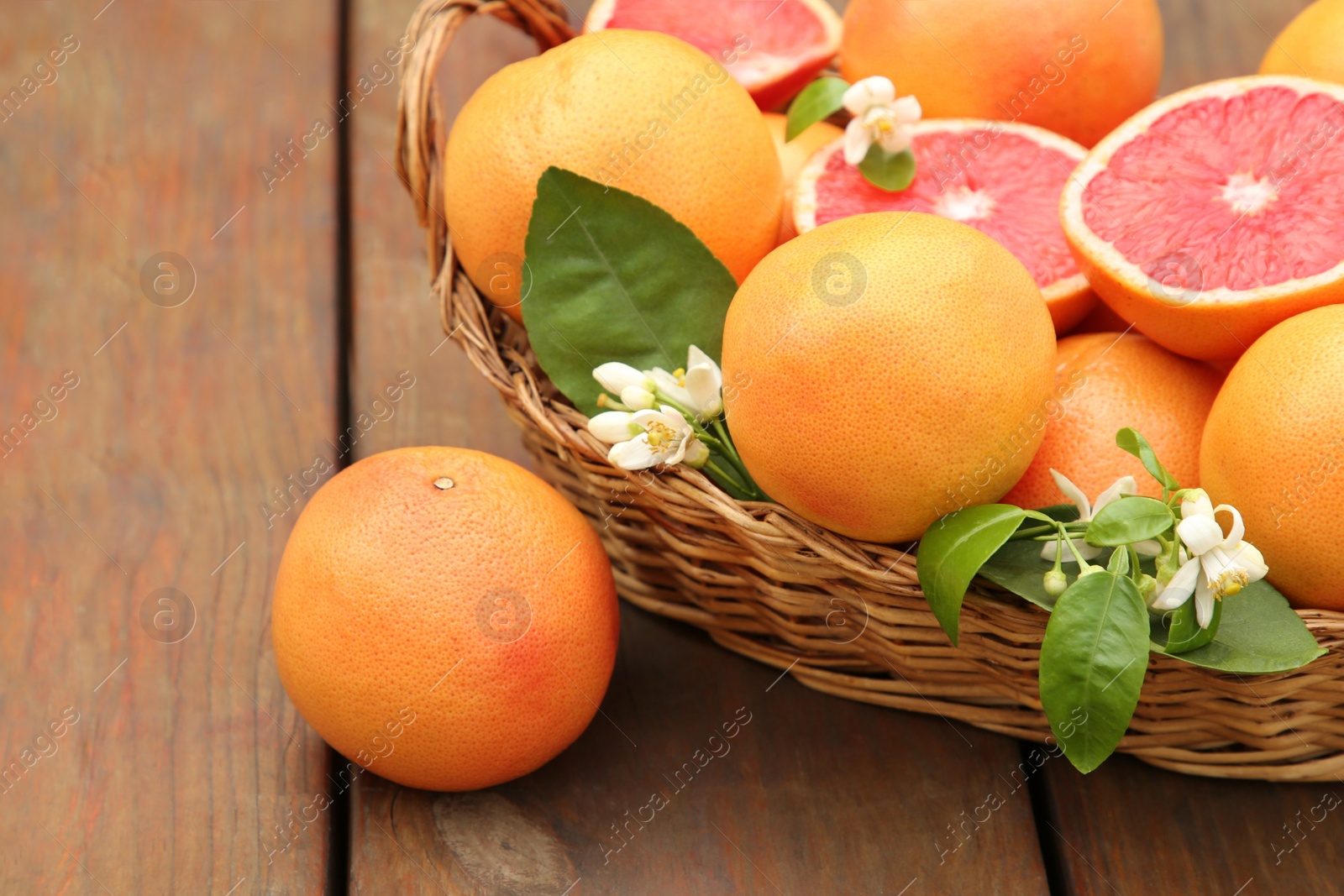 Photo of Wicker basket with fresh grapefruits and green leaves on wooden table