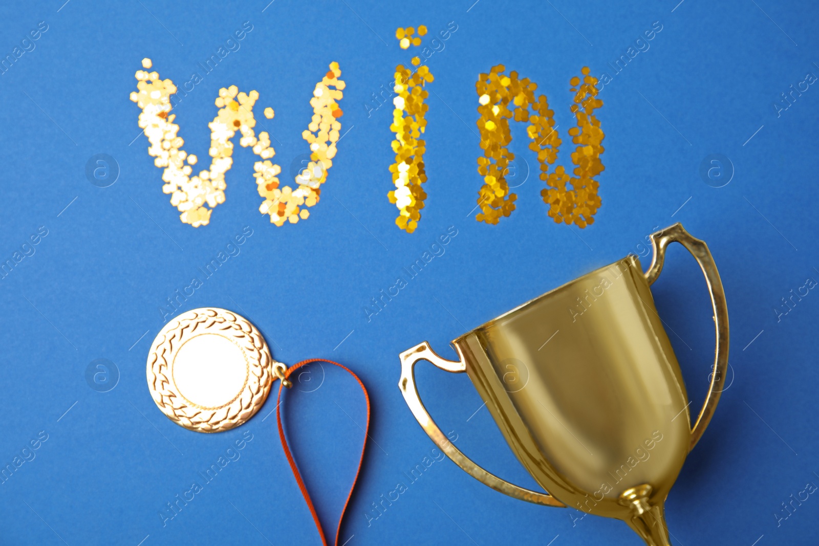 Photo of Gold trophy cup, medal and word WIN made with confetti on blue background, flat lay