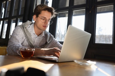 Photo of Teenage student with laptop studying at table in cafe