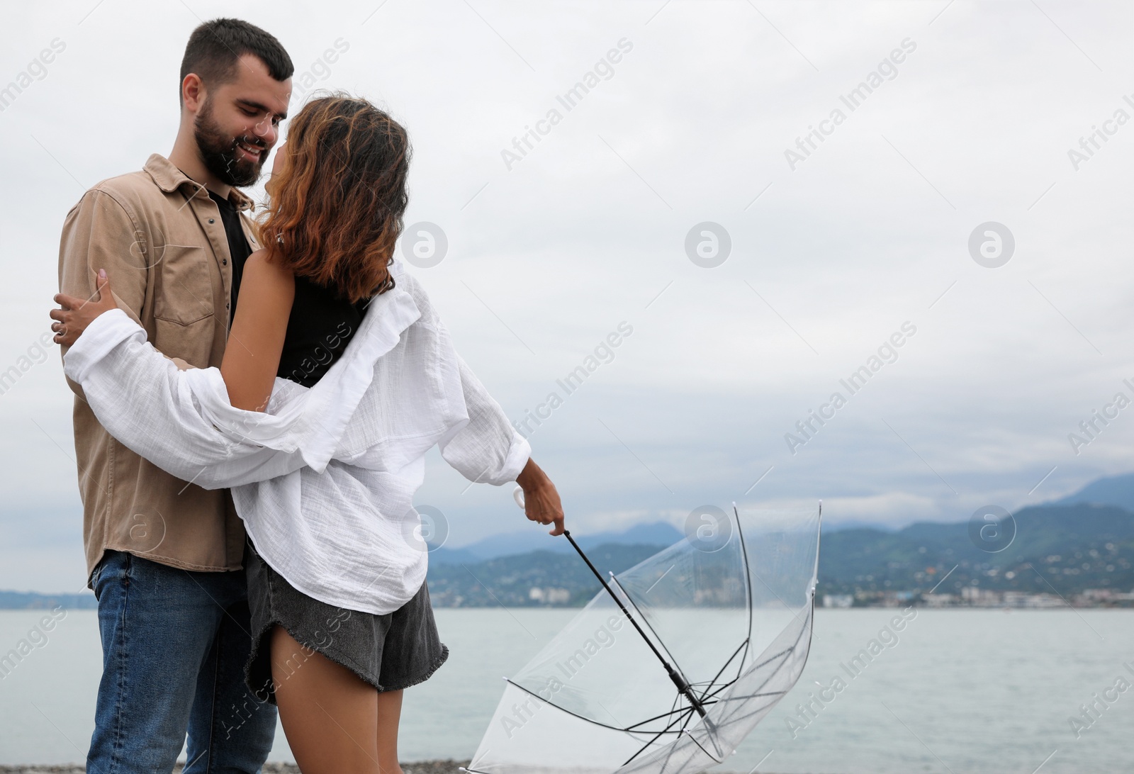 Photo of Young couple with umbrella enjoying time together under rain on beach, space for text