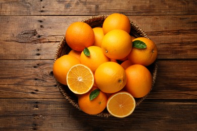 Photo of Many ripe oranges and green leaves on wooden table, top view