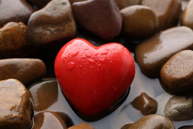 Red decorative heart on stones and water, closeup