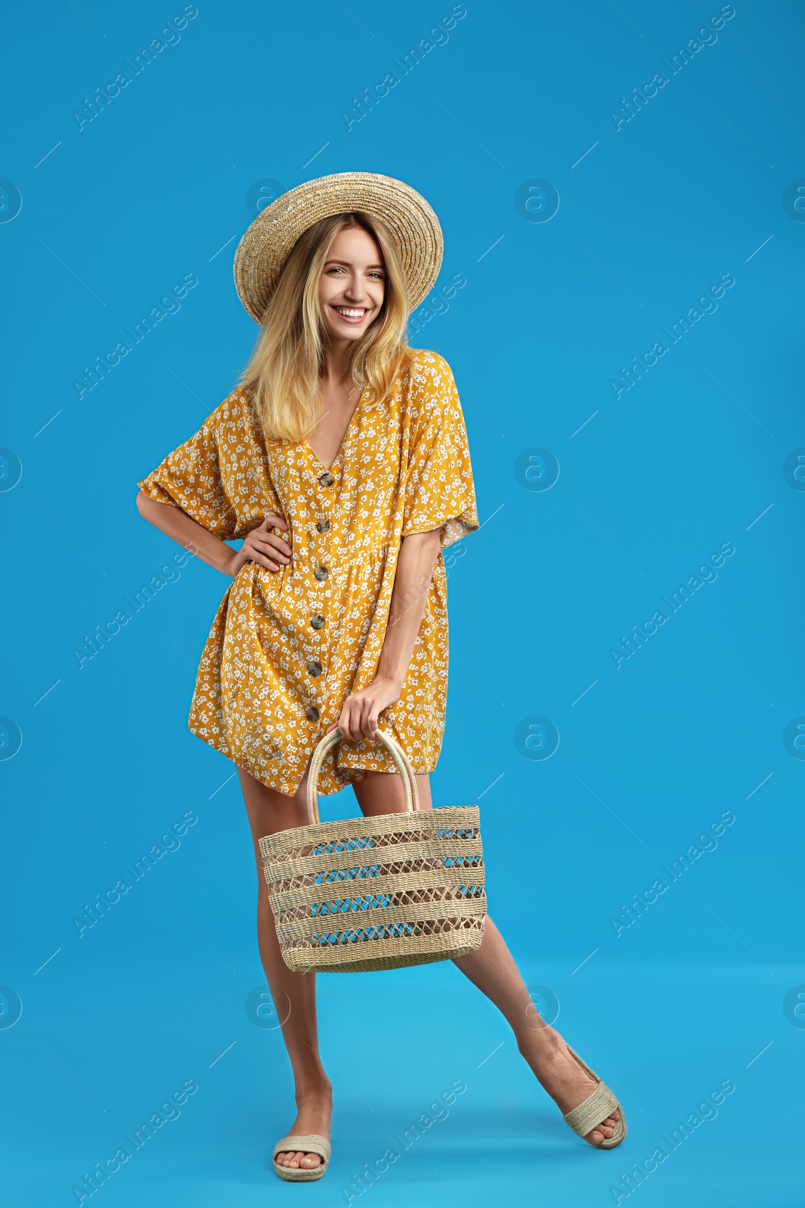 Photo of Young woman wearing stylish dress with straw bag on blue background