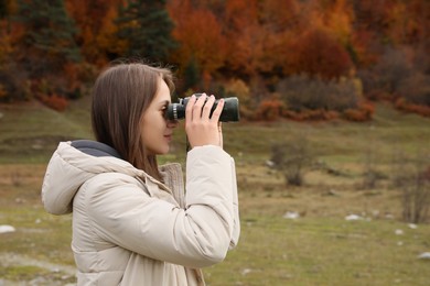 Woman looking through binoculars in beautiful mountains. Space for text