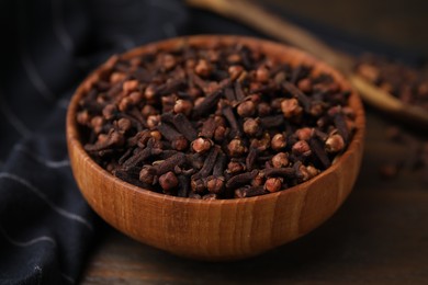 Aromatic cloves in bowl on wooden table, closeup