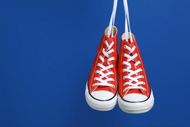 Photo of Pair of new stylish red sneakers hanging on laces against blue background. Space for text