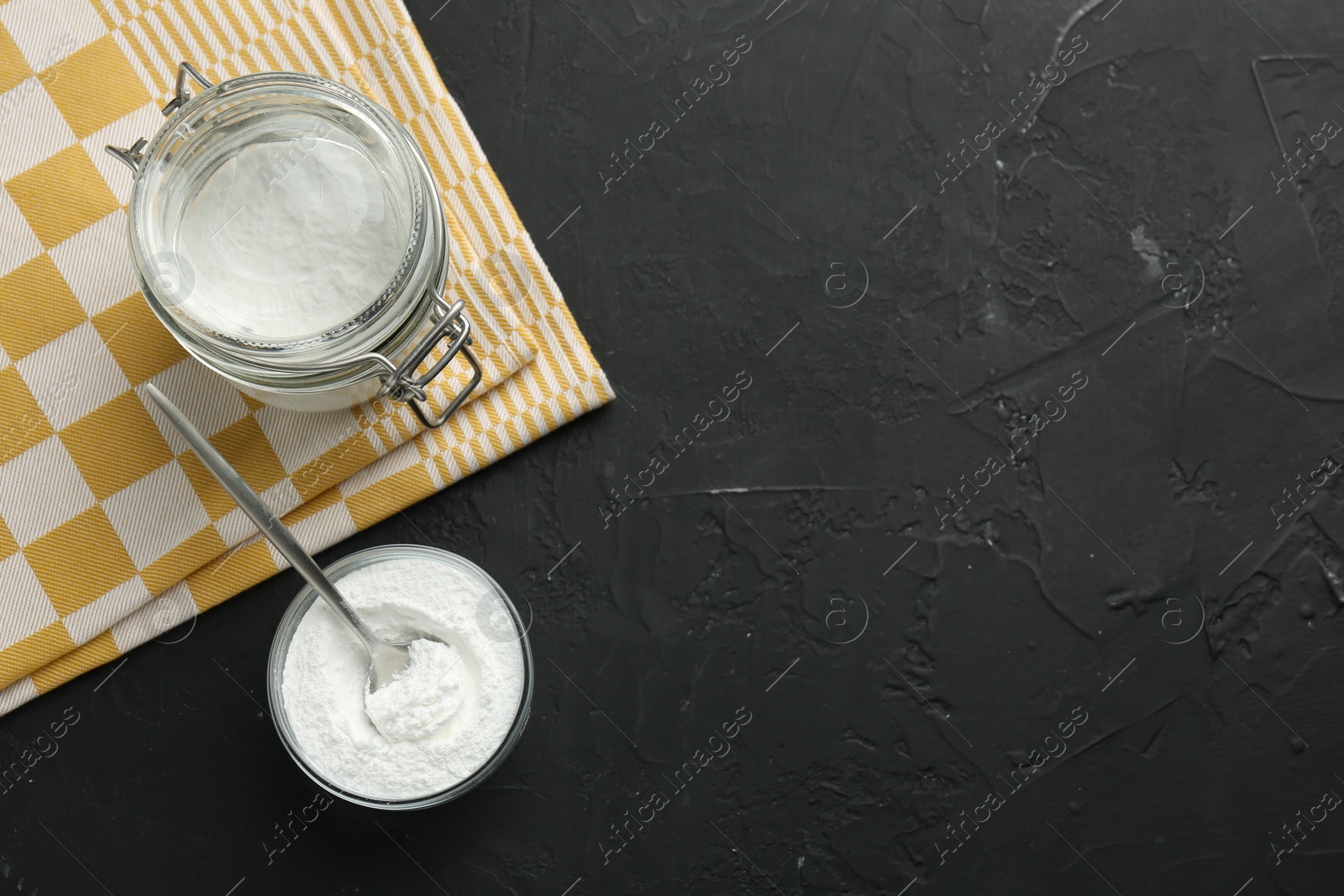 Photo of Baking powder in bowl and jar on black textured table, flat lay. Space for text